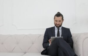 Beard Man in Black Suit Sitting on White Couch