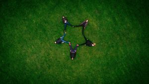 five people laying on grass field making star sign