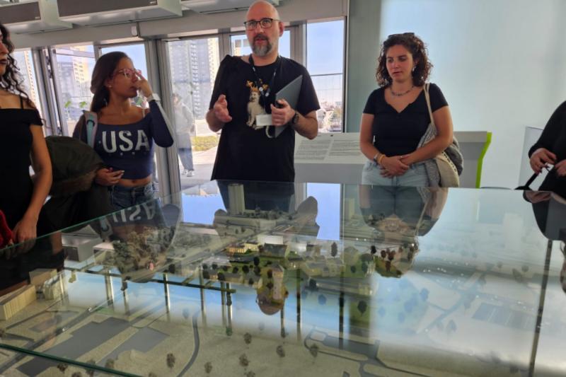 Lecturer showing a town model display to students standing around a display