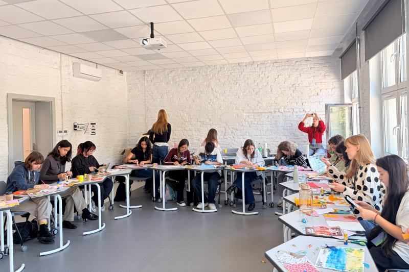 Students sit at desks arranged in a circle and work on their artworks in classroom